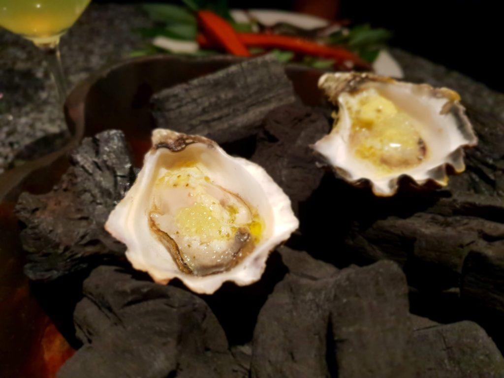 alt="oysters presented on a charcoal filled platter in a fine dining restaurant"