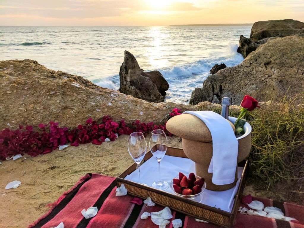alt="romantic evening with red roses and wine by the sunset on the beach"